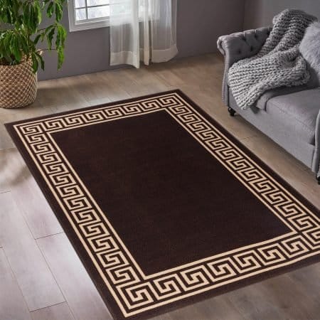 Greeky Rugs shown in multiple two-tone colourways including Beige & Black, Black & White, Blue & Cream and Red & Black, plus solid Navy and Pink, across UK room settings from a doorway accent to a hallway runner, illustrating the collection's eight available sizes from 40×60 cm to 80×300 cm.